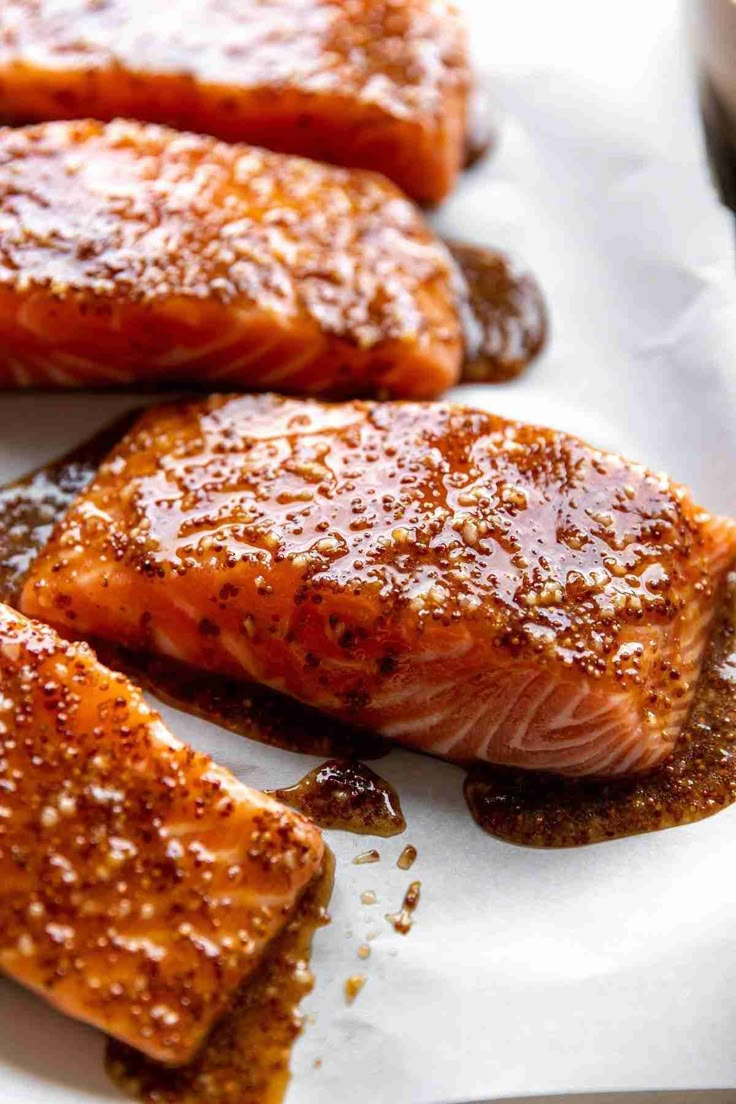 three salmon fillets on a white plate with brown sauce and seasoning next to them