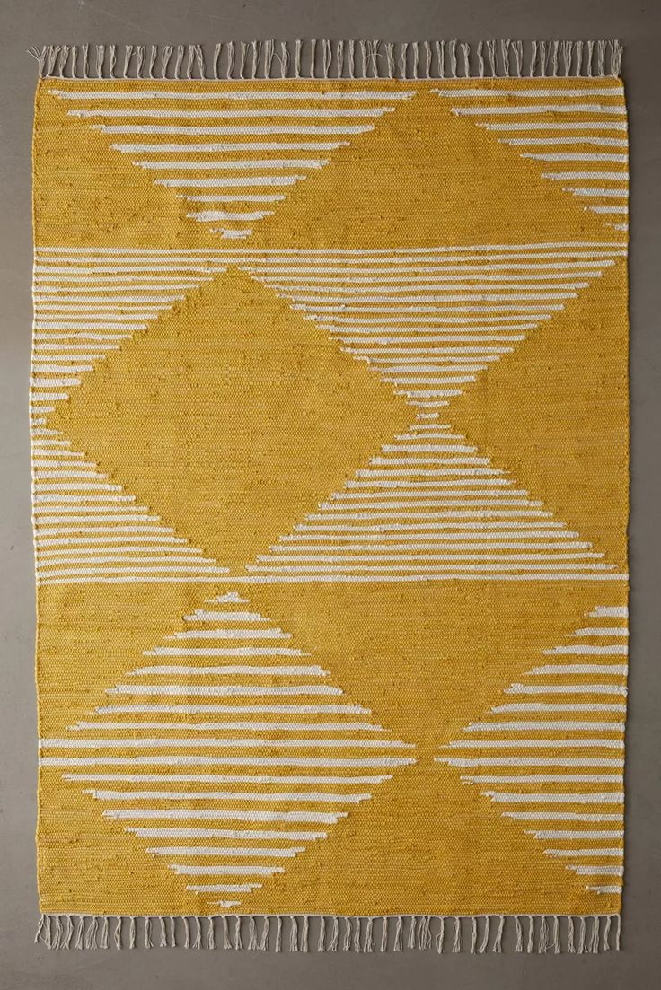 a yellow and white rug with stripes on the bottom, in front of a gray wall