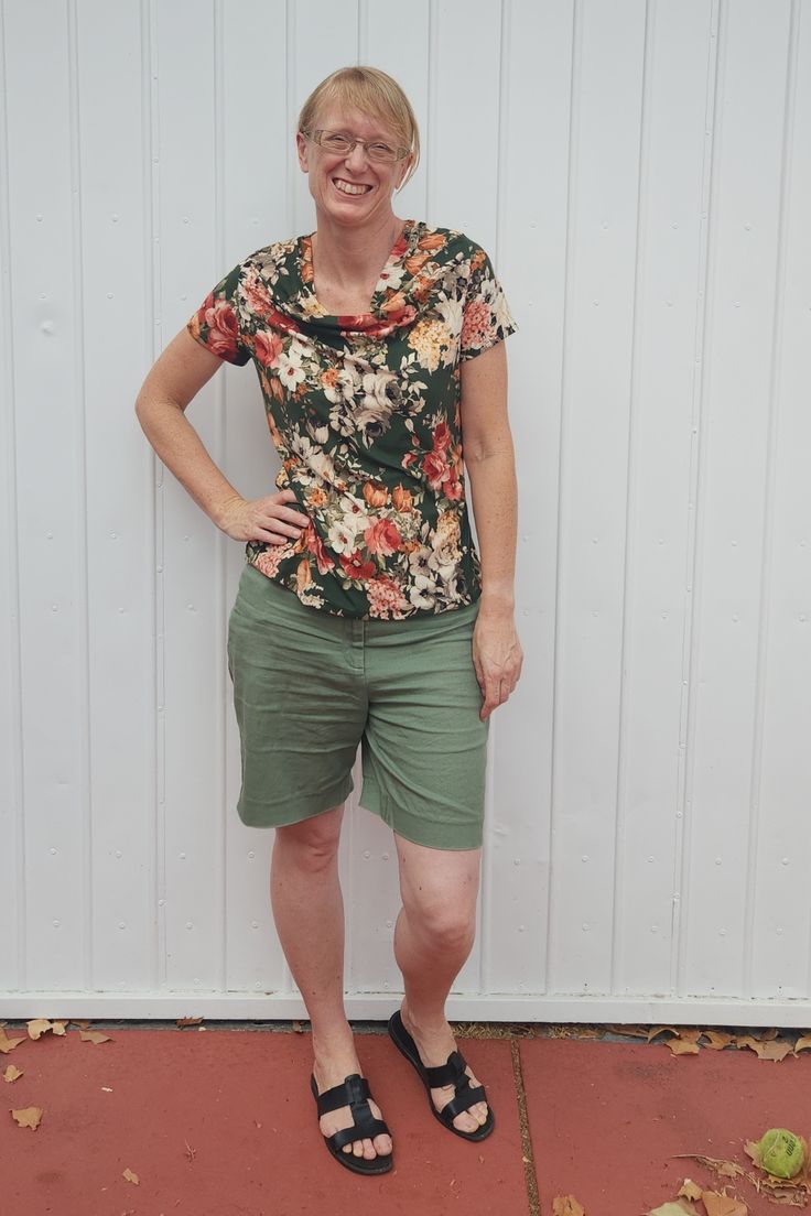 a woman standing in front of a white wall wearing green shorts and a floral shirt