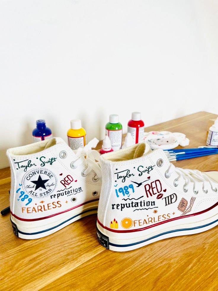 two pairs of white shoes sitting on top of a wooden table next to markers and pencils