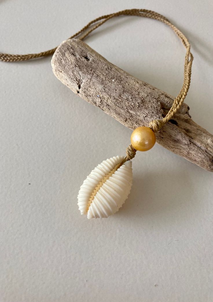 Hawaiian endemic cowrie shell (Granulated Cowrie) paired with a gold freshwater pearl on braided waxed twine. 19 inch cord and fitted with a puka shell closure. The braided waxed twine chain is durable and can be worn in the ocean as well as in other active pursuits! Natural Handmade Adjustable Shell Necklace, Handmade Adjustable Natural Shell Necklace, Adjustable Natural Cowrie Shell Necklace, Handmade Adjustable Natural Shell, Shell Jewelry With Adjustable Cord For Vacation, Shell-shaped Adjustable Cord Jewelry For Vacation, Shell-shaped Jewelry With Adjustable Cord As Gift, Adjustable Natural Shell Necklace As Gift, Adjustable Shell-shaped Jewelry Cord As A Gift