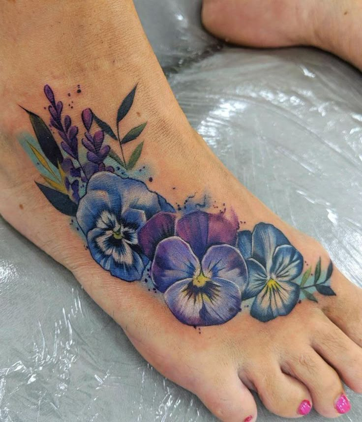 a foot tattoo with blue and purple flowers on it