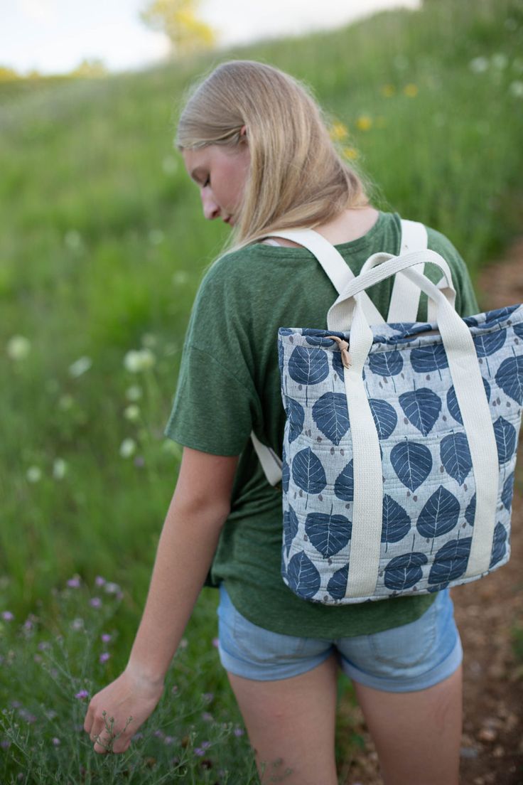 a woman carrying a blue and white tote bag on her back in a field