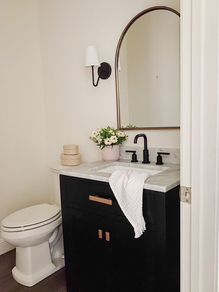 a white toilet sitting next to a black sink in a bathroom under a large mirror