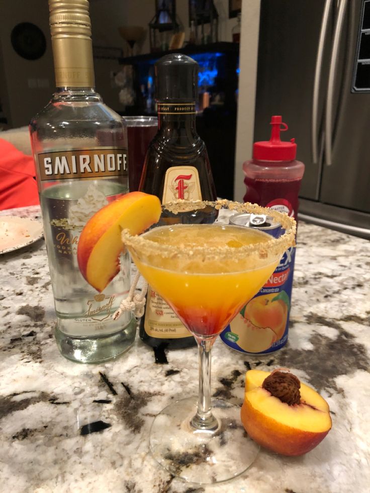 an orange martini sits on the counter next to two bottles of vodka and peaches