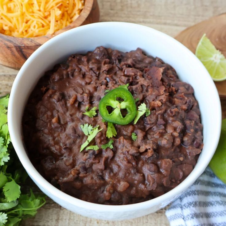 a white bowl filled with black beans and topped with green peppers, cilantro and shredded cheese