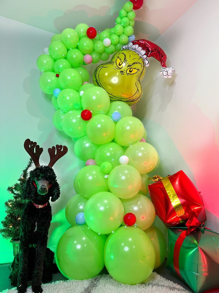 a bunch of balloons that are in the shape of a christmas tree and a dog standing next to it