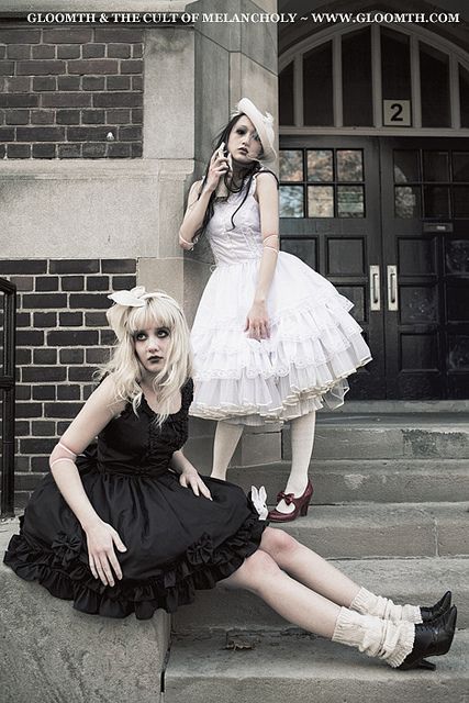 two women dressed in gothic clothing sitting on steps talking on their cell phones and posing for the camera