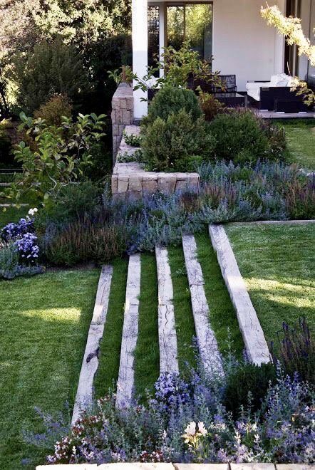 an outdoor garden with steps leading up to the house and flowers growing on the lawn