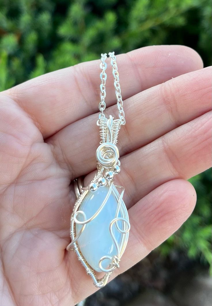 This diamond shaped opalite pendant is wrapped in silver wire and adorned with silver beads and a beautiful swirl on top. Handmade jewelry is one of the best gifts! Opalite is deigned to mimic the October birthstone, natural opal, so this would be the perfect gift for those you know born in October. The pendant comes with a complimentary chain. Teardrop Agate Wire Wrapped Jewelry, Wire Wrapped Teardrop Agate Jewelry, Handmade Silver Moonstone Crystal Necklace, Silver Opal Wire Wrapped Necklace, Bohemian Chalcedony Wire Wrapped Jewelry, Bohemian Wire Wrapped Chalcedony Jewelry, Handmade Silver Teardrop Pendant Crystal Necklace, Handmade Silver Crystal Necklace With Teardrop Pendant, Moonstone Wire Wrapped Jewelry Gift