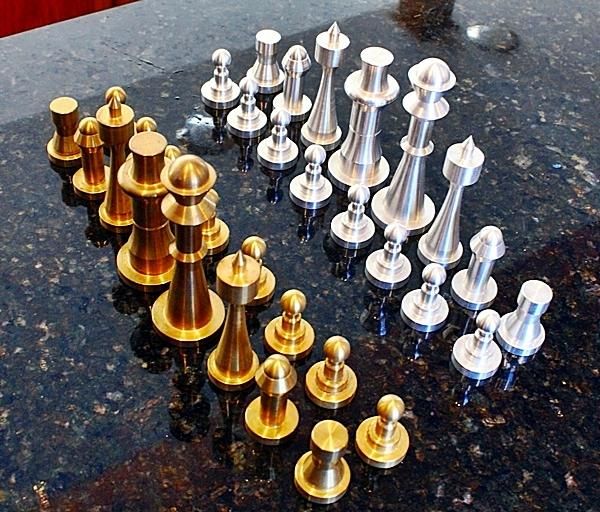 an assortment of brass and silver chess pieces on a black marble counter top with red curtains in the background