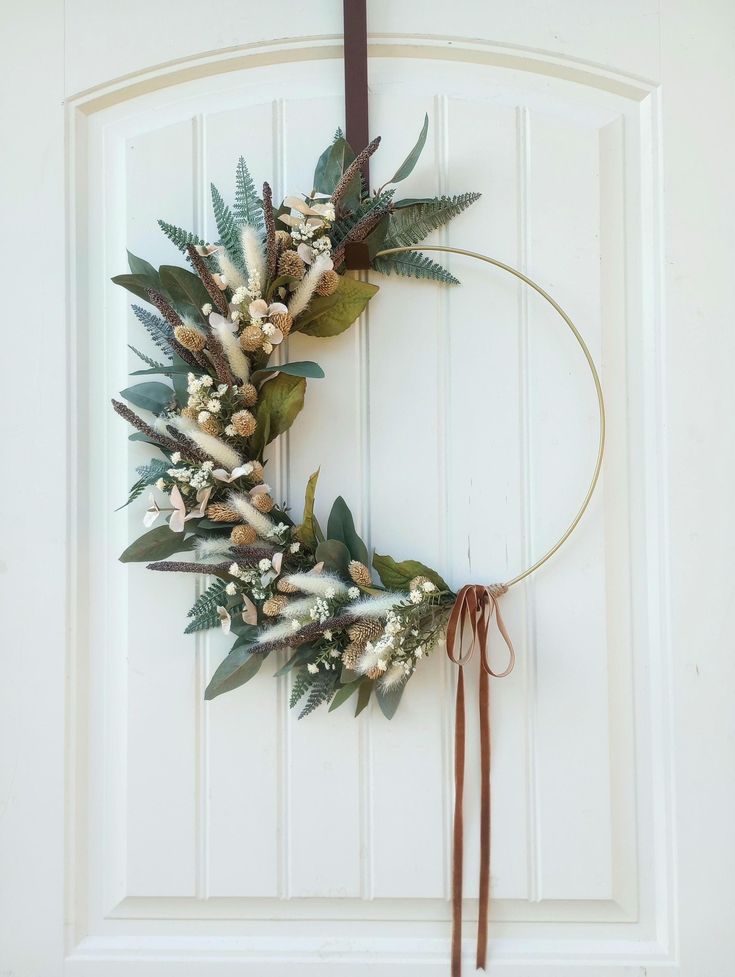 a wreath hanging on the front door with flowers and greenery around it's edges