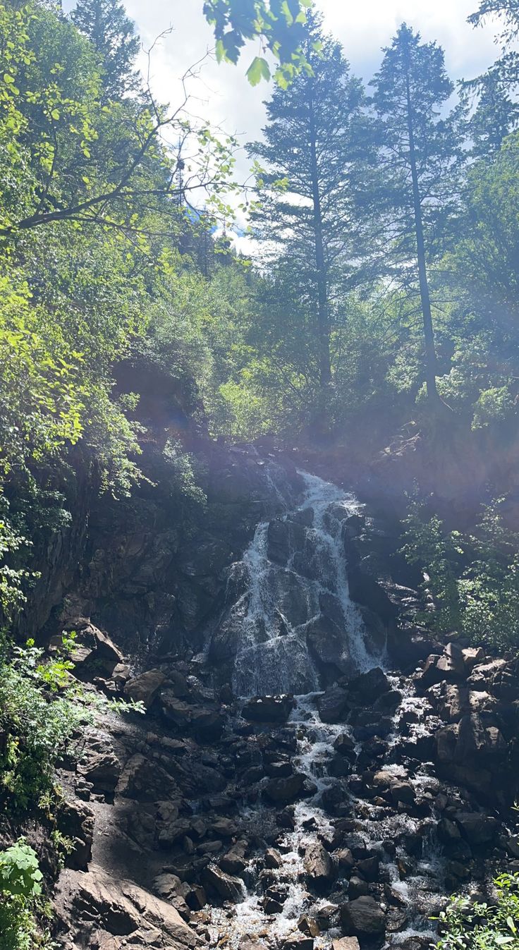 the sun shines on a small waterfall surrounded by trees