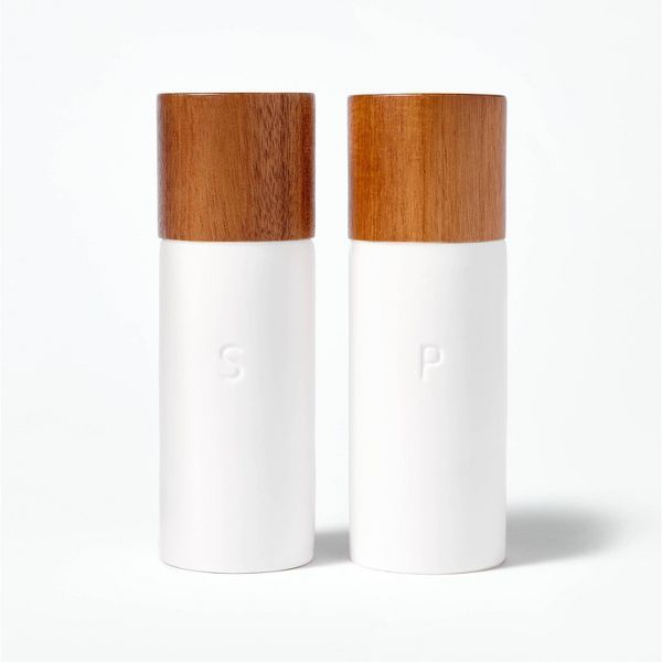 two white salt and pepper shakers with wooden tops on a white background, one is empty