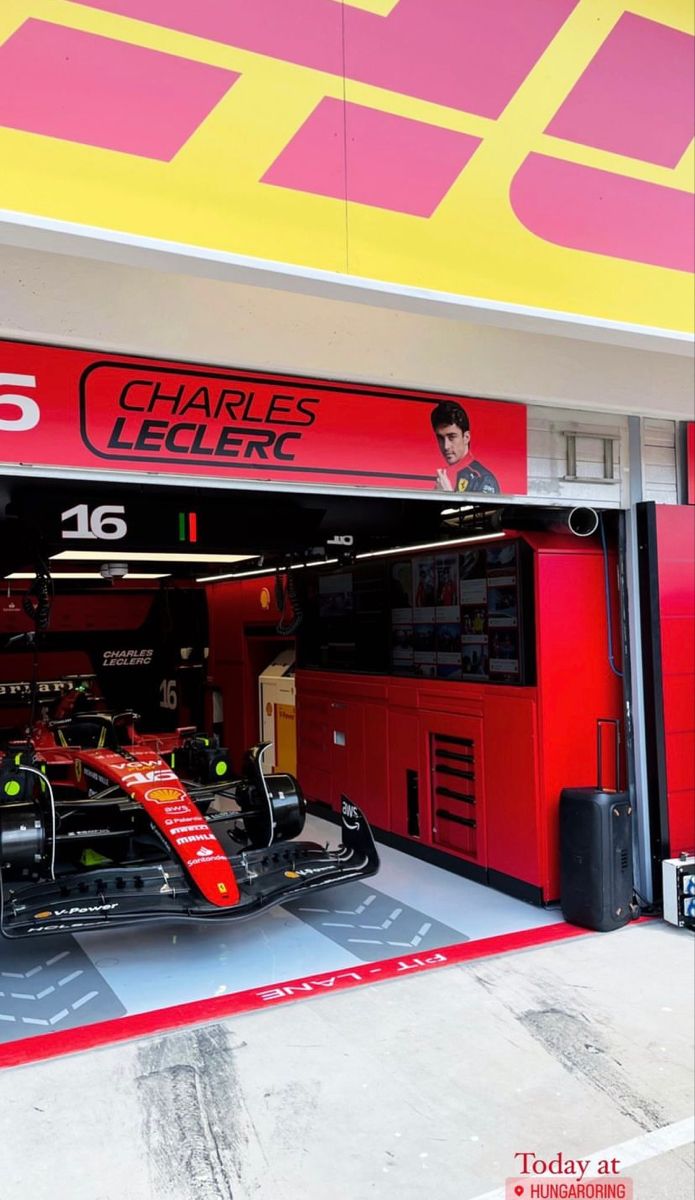 a race car sits in the garage of a racing team's garage, which is painted red and yellow