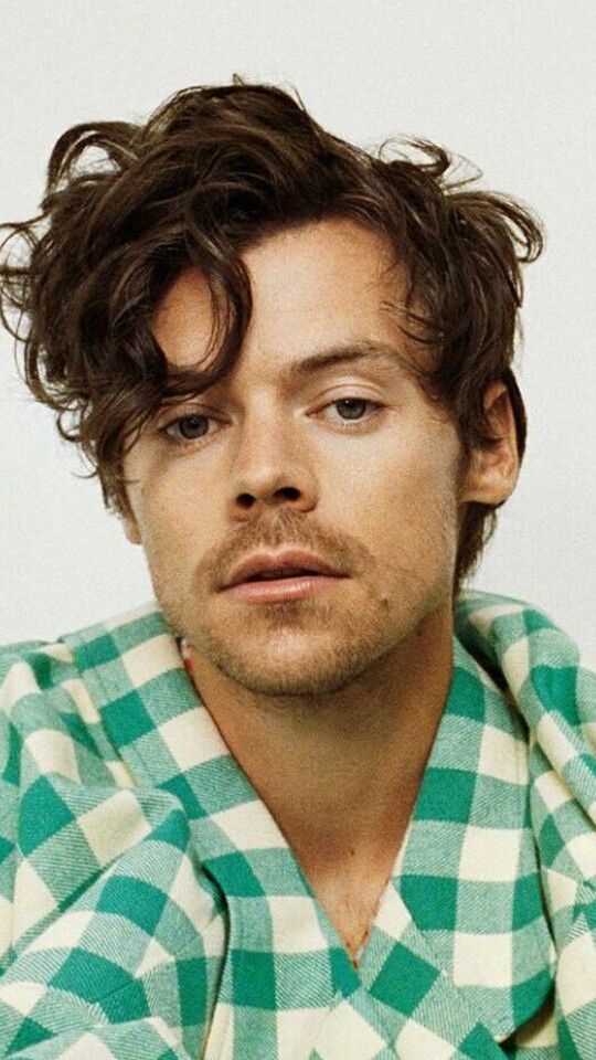 a man with curly hair wearing a green and white checkered shirt looking at the camera