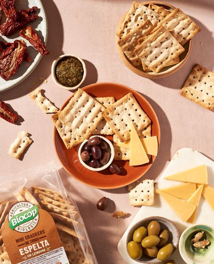 an assortment of crackers, olives and cheese on a table with other snacks