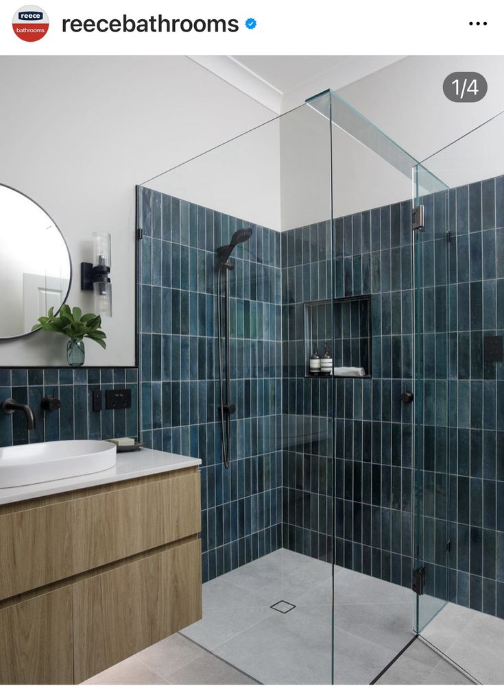 a blue tiled bathroom with a shower and sink in the corner, next to a mirror