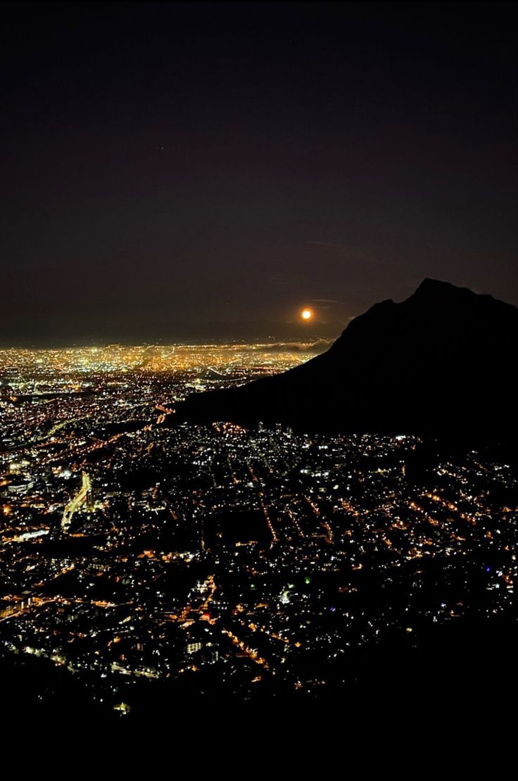 the city lights are lit up in the night sky over a large mountain and valley