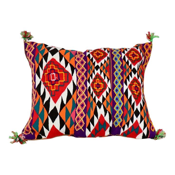 an orange, red and black pillow with tassels on the edges is shown