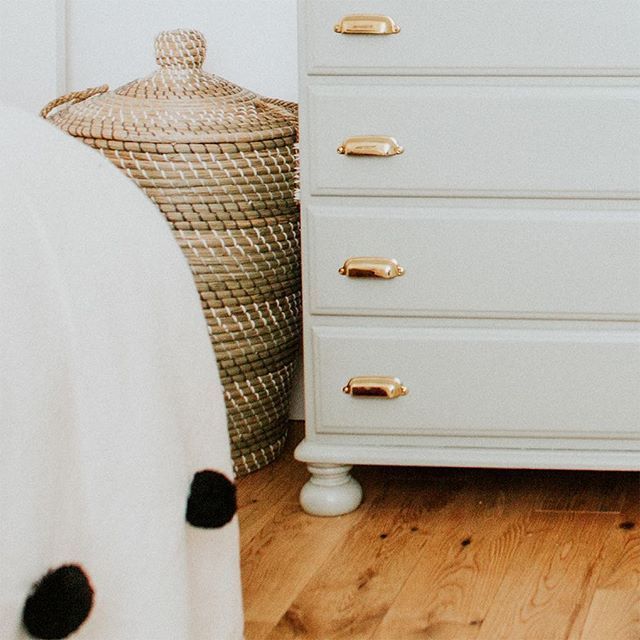 a white chest of drawers sitting next to a basket on top of a wooden floor