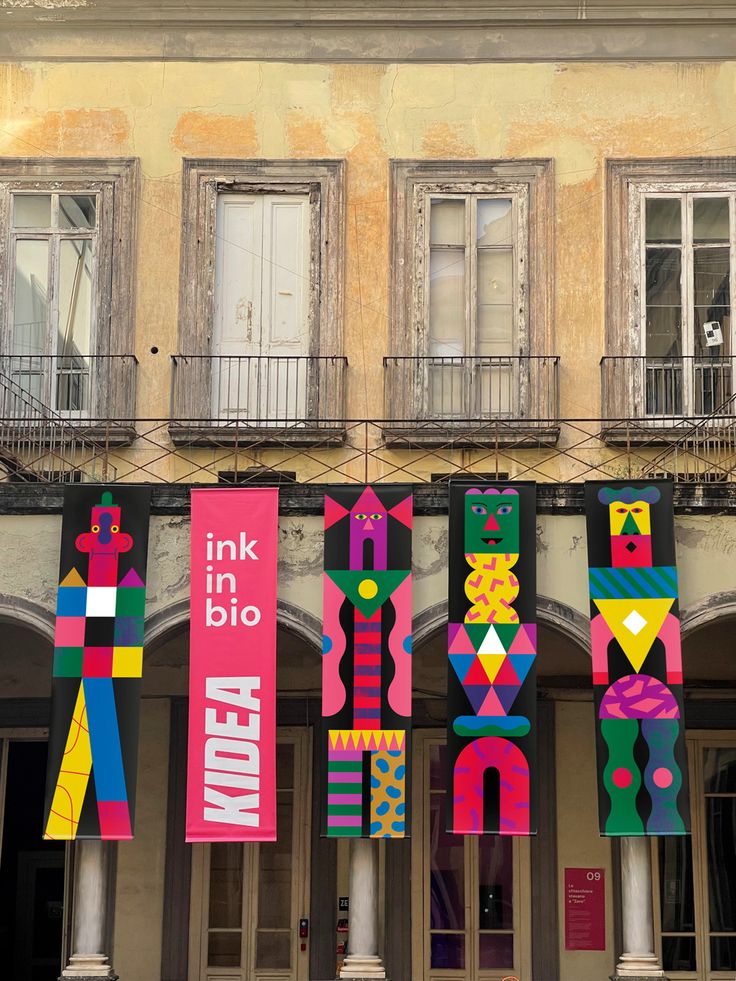 several colorful banners hanging from the side of a building with balconies and windows