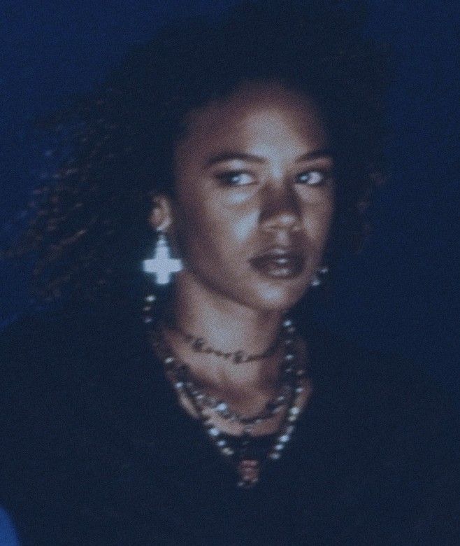 a woman with large earrings on her neck looking at the camera while standing in front of a dark background