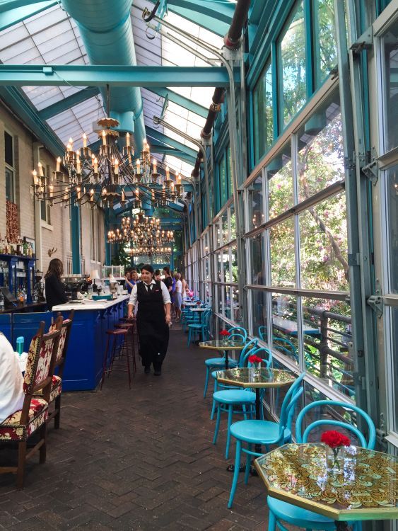 the inside of a restaurant with many tables and chairs in front of windows that have chandeliers hanging from them