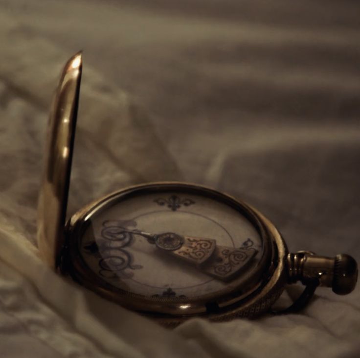 an antique pocket watch is lying on the bed sheet with its reflection in it's case