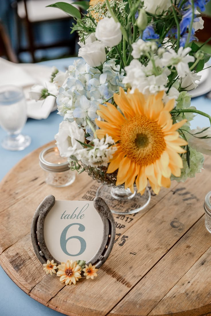 a wooden table topped with a vase filled with white and yellow flowers next to a number six sign