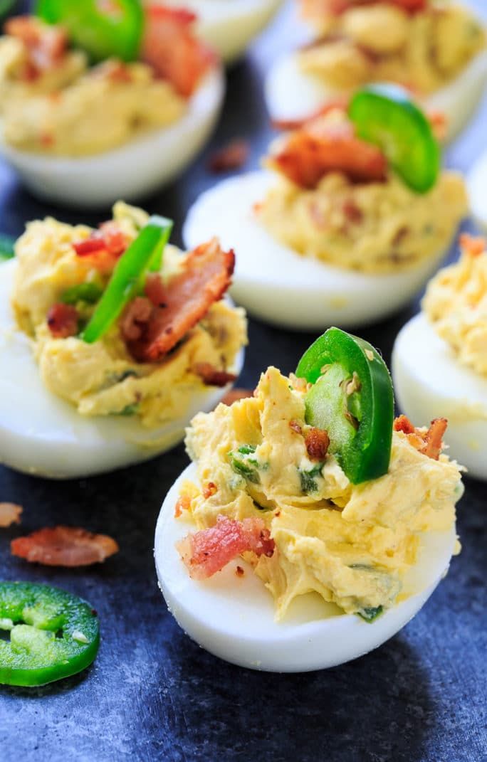 deviled eggs with bacon, jalapenos and green peppers on a blue surface