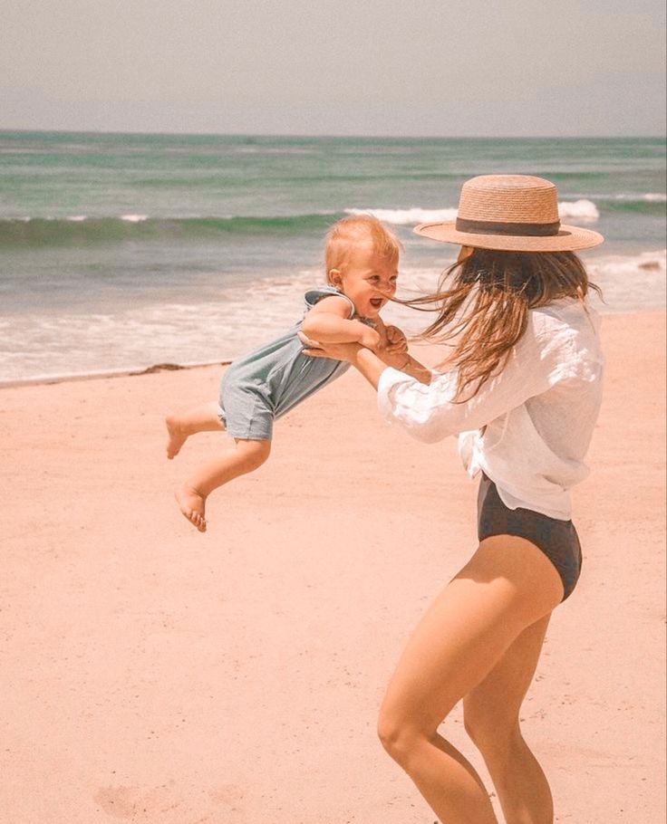 a woman holding a baby on the beach playing with a frisbee in front of the ocean