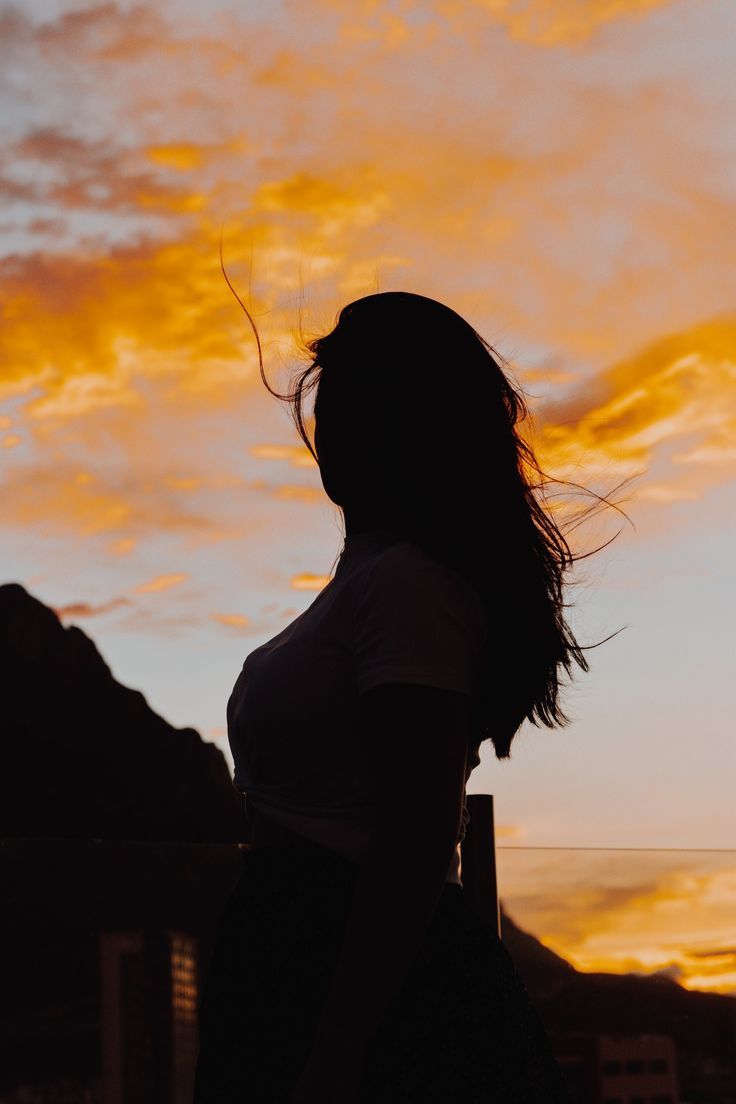 a woman standing in front of a sunset with her hair blowing in the wind,