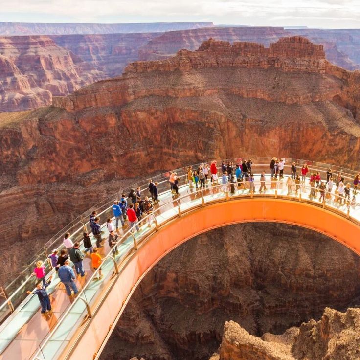 many people are standing on the edge of a bridge over looking the grand canyon below