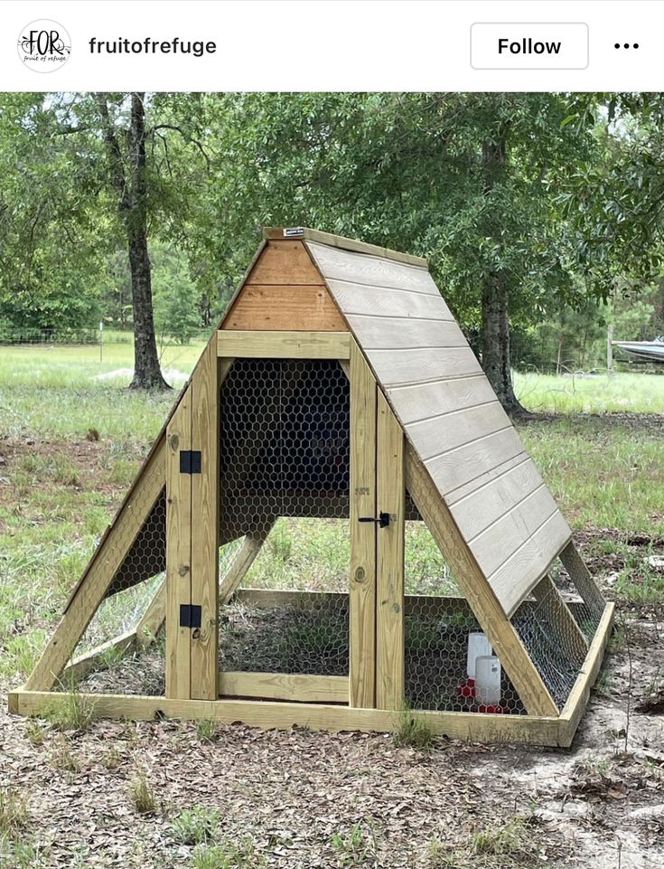 a chicken coop in the middle of a field with trees and grass behind it,