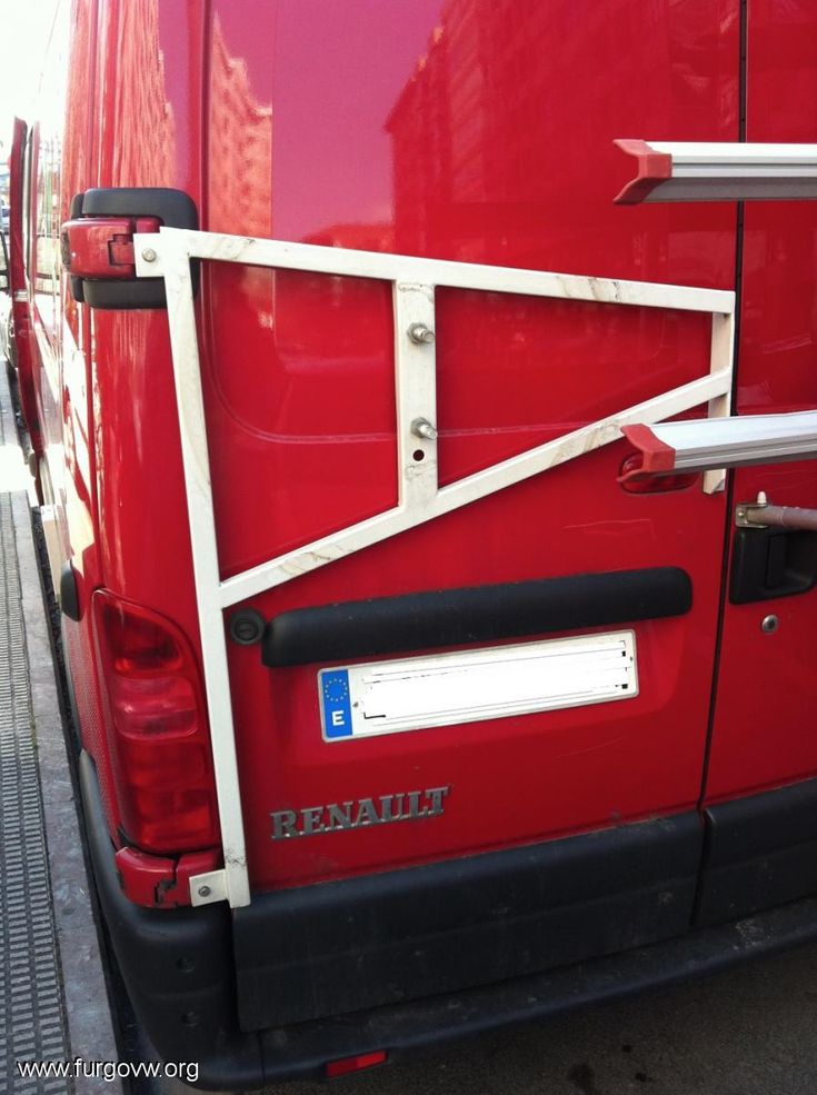 the rear end of a red van with a metal bar on it's side