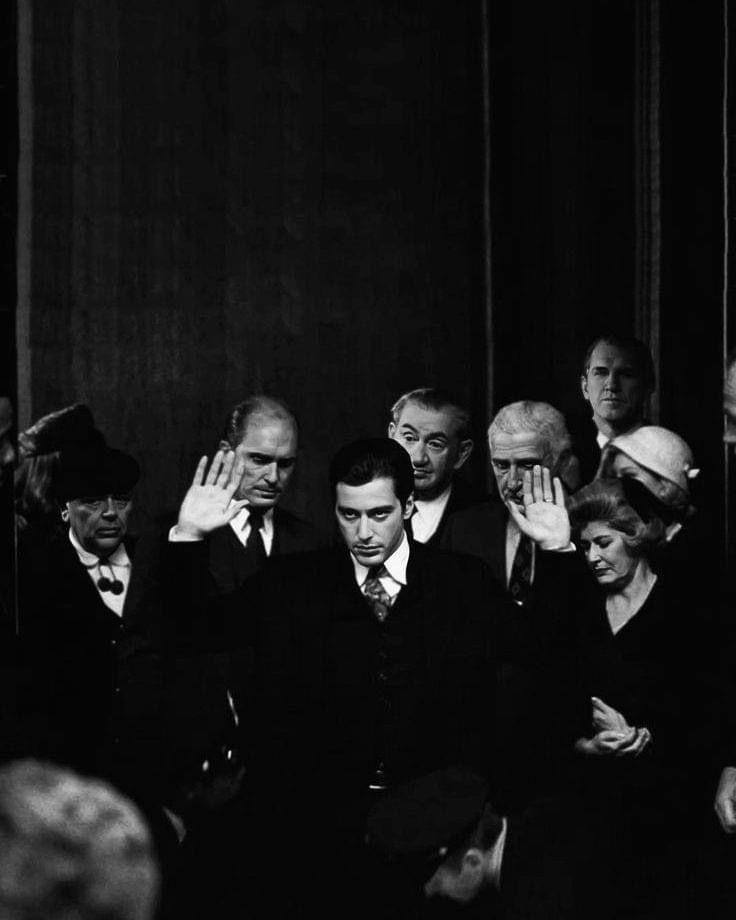 a black and white photo of men in suits with their hands on their faces, surrounded by other people