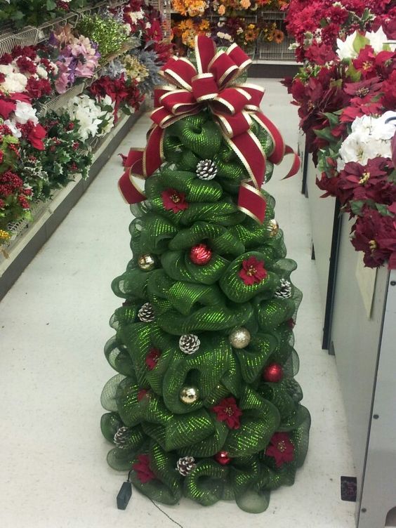 a green christmas tree with red and white ornaments on it in a flower store aisle