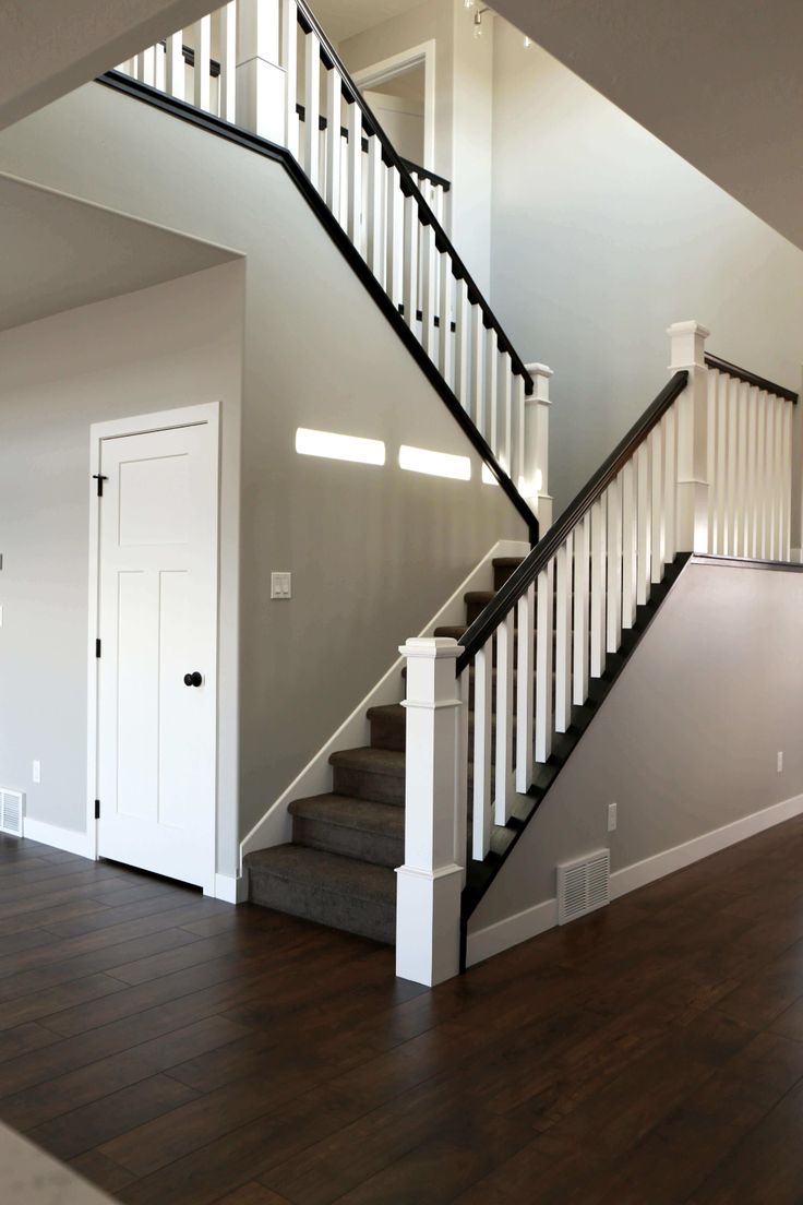 a white staircase with black railing and wood flooring in an empty room next to a door