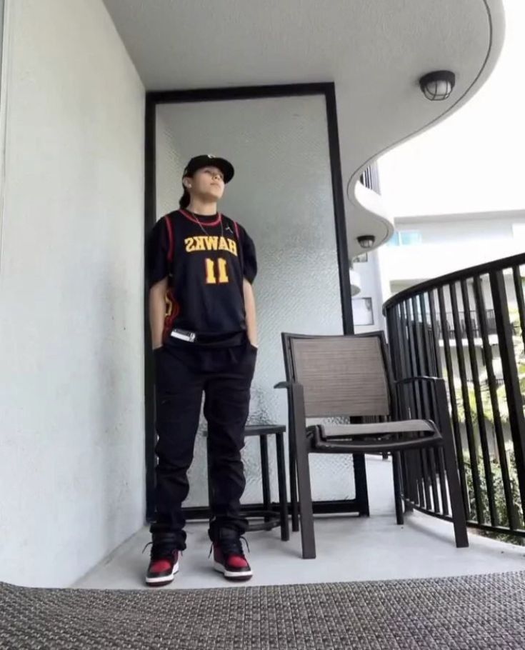 a young man standing in front of a door wearing a baseball jersey and black pants