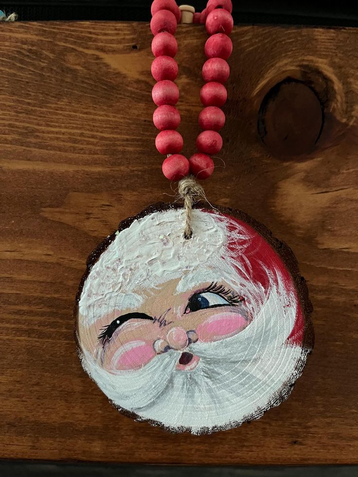 a santa clause ornament hanging from a wooden table with beads on the string