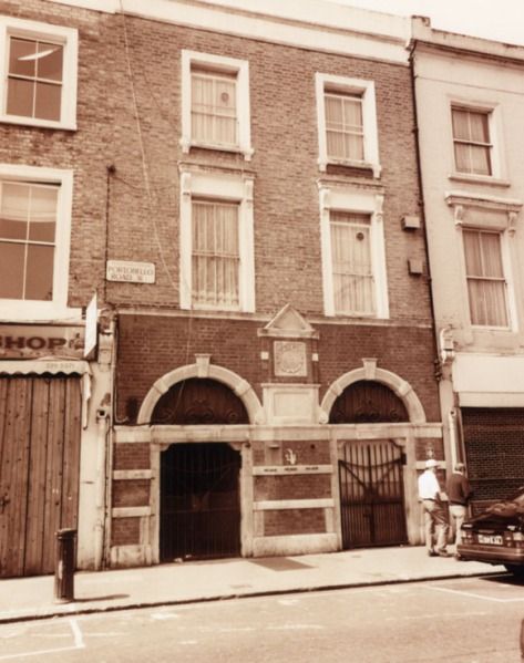 an old brick building with two men standing in front of it and cars parked on the street