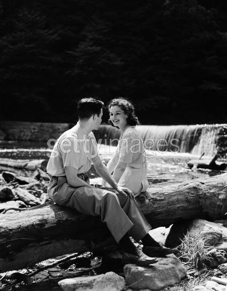 a man and woman sitting on top of a log next to a waterfall