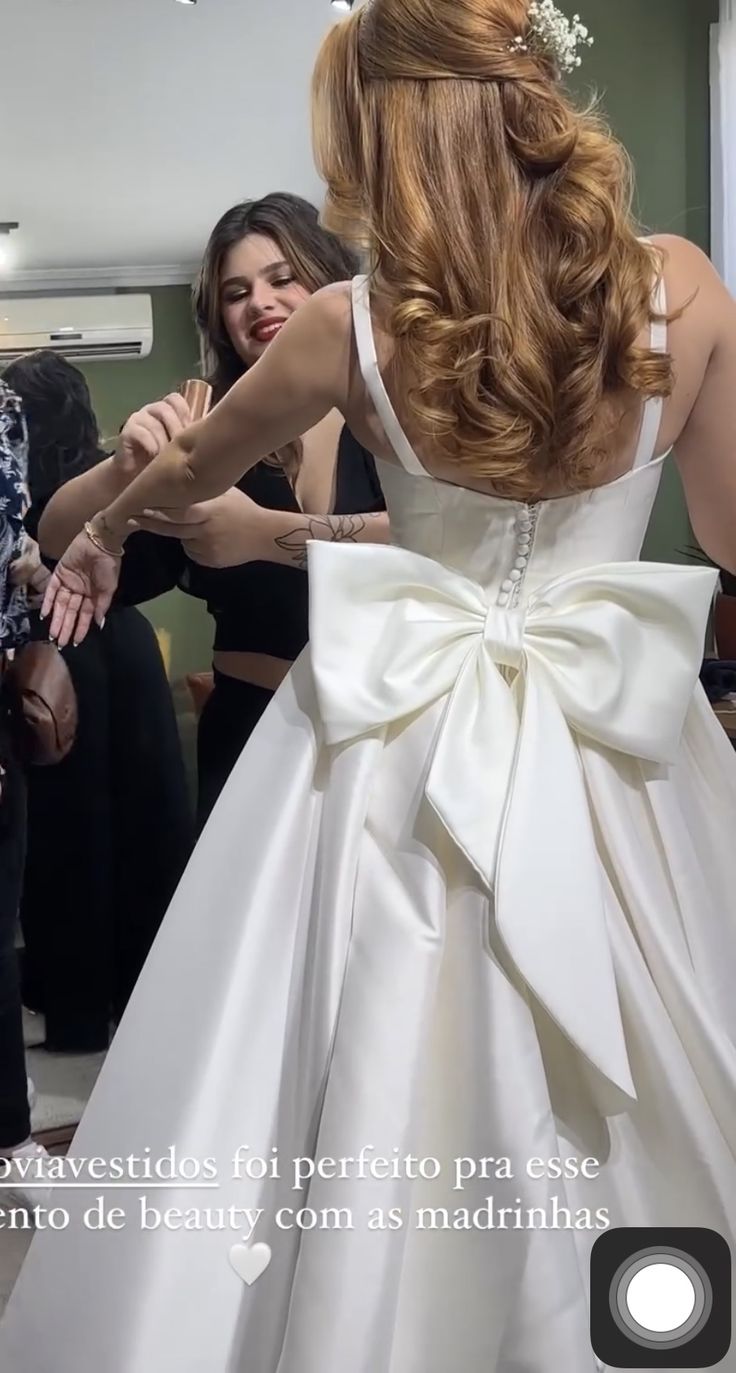 a woman in a white wedding dress with a big bow on her back and people around her