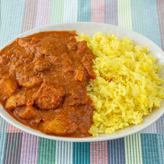 a white plate topped with rice and meat next to another plate filled with food on a colorful table cloth