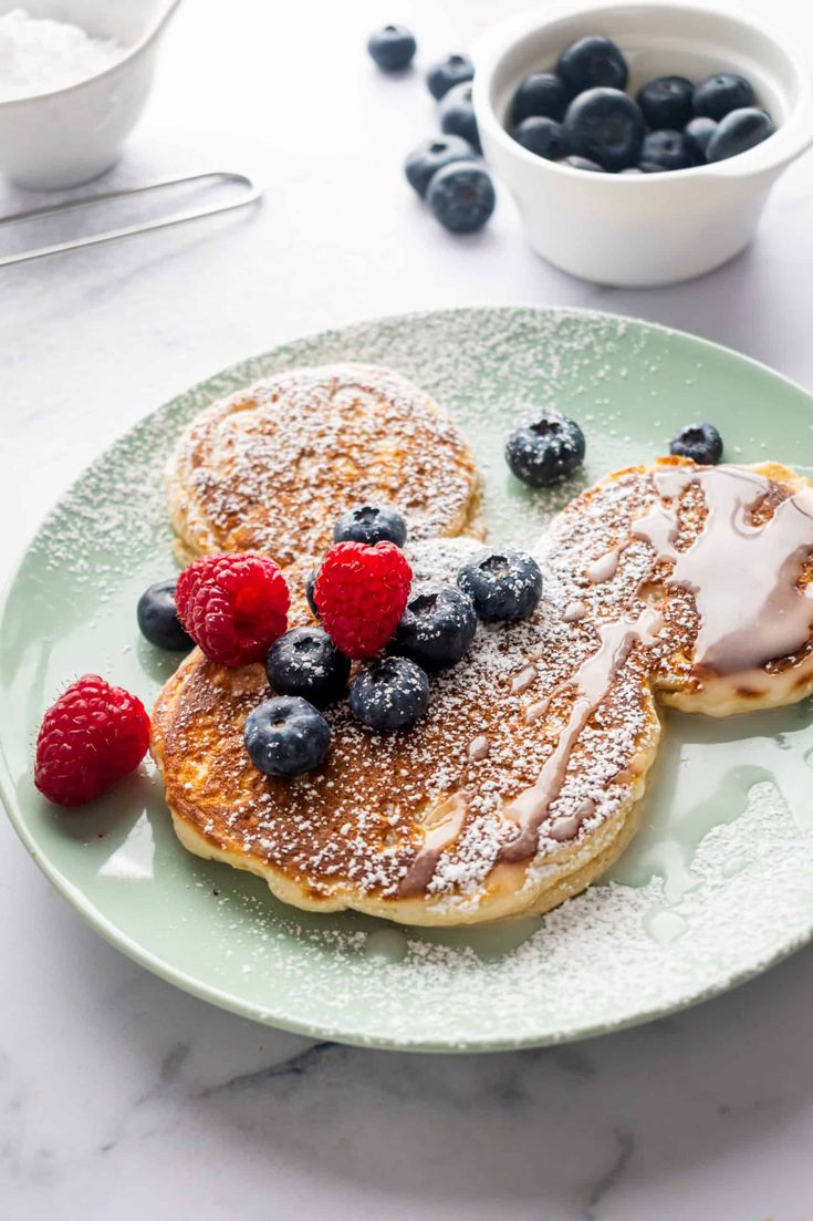 two pancakes on a plate with berries and powdered sugar