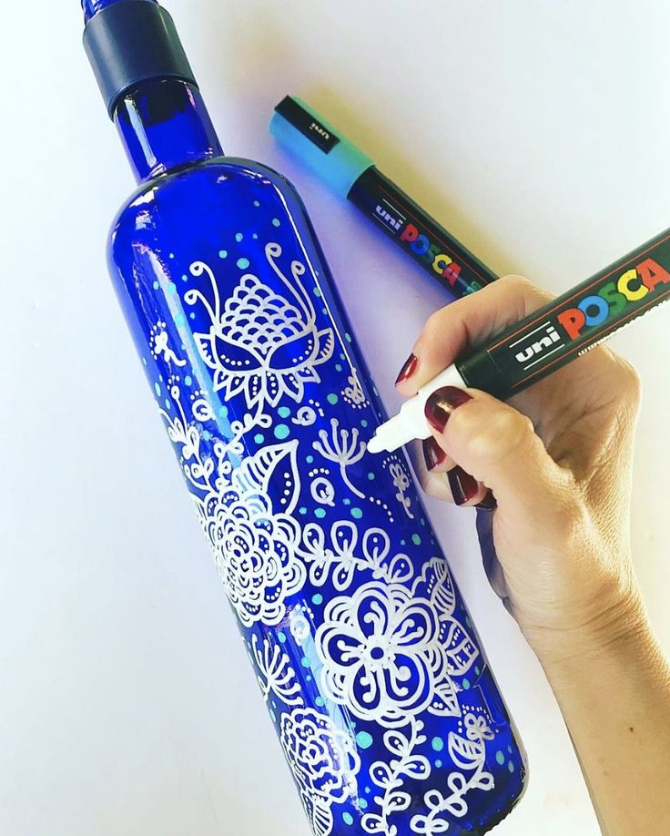 a woman is holding a blue bottle with white designs on it and two crayons next to it