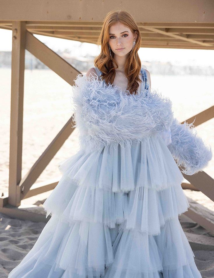 a woman standing on top of a sandy beach wearing a blue dress with ruffles