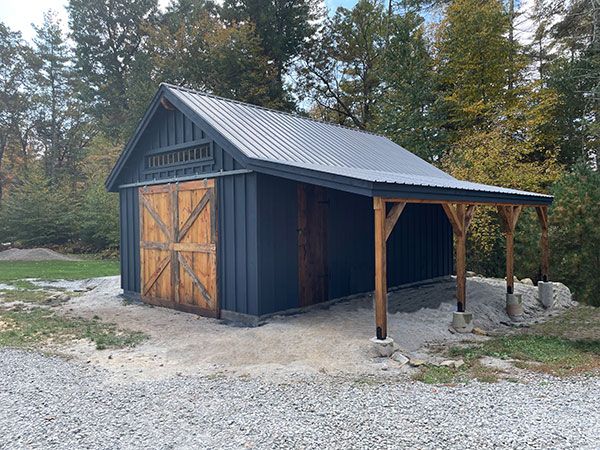 a blue barn with a metal roof in the middle of gravel and trees behind it