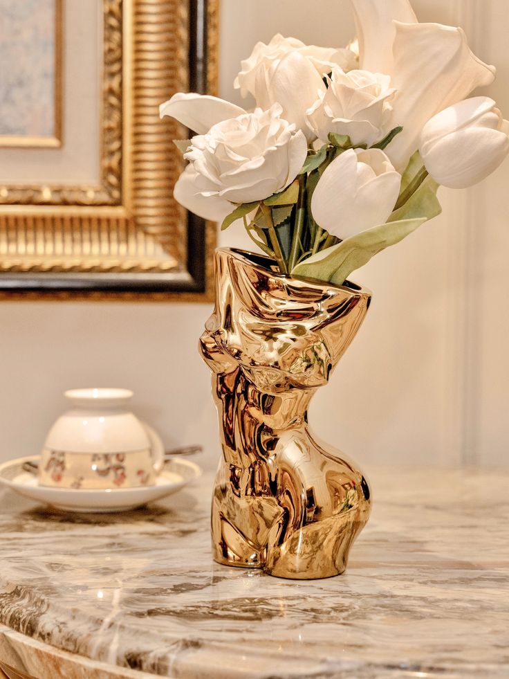 a gold vase filled with white flowers on top of a marble table next to a mirror